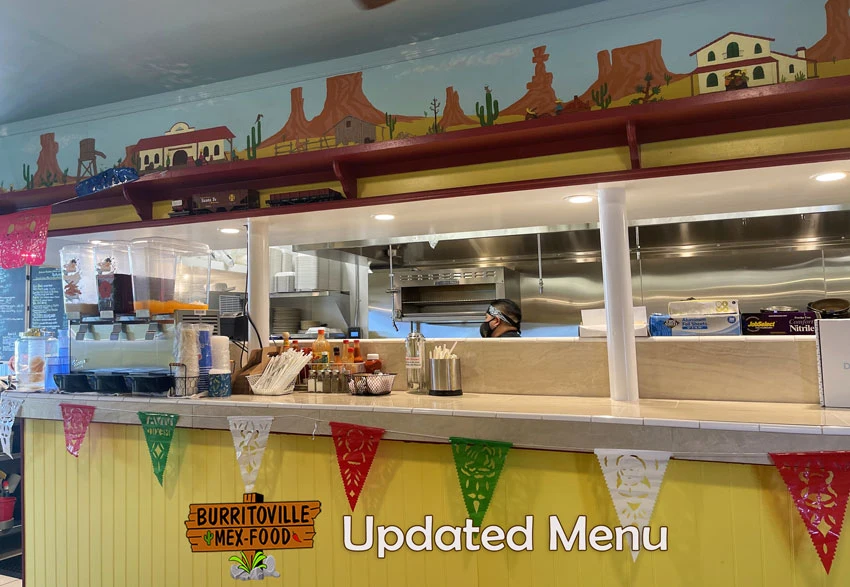 BurritoVille Mex Food - New Menu for 2023 - Man behind BurritoVille Mex Food Counter, logo and texts.